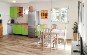 A modern kitchen with green cabinets, a stainless steel refrigerator, and a dining area with a table and chairs.