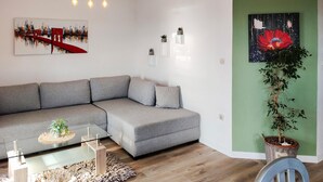 Un salon moderne avec un canapé d’angle gris, une table basse en verre et un mur d’accent vert.