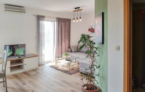 A modern living room with a flat-screen TV, a glass coffee table, a sofa, and a potted plant.