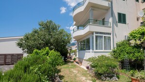 Un immeuble résidentiel à plusieurs étages, doté de balcons, d’un espace jardin avec différentes espèces de plantes et surplombant un ciel dégagé.