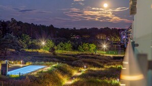 Vista nocturna de un hotel con piscina, rodeado de senderos iluminados y un área boscosa.