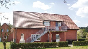 Une maison à deux étages, construite en briques, avec un toit recouvert de tuiles, un balcon doté d’une rambarde en métal et un petit escalier menant à l’étage supérieur.