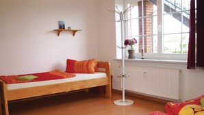 Une petite pièce agréable, dotée d’un lit simple, d’un radiateur, d’une fenêtre donnant sur un beau paysage et d’une étagère sur laquelle se trouvent un livre et une horloge.