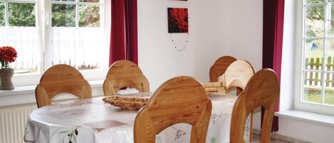 Un comedor con una mesa redonda, seis sillas de madera, un jarrón con flores y dos cuadros en la pared.