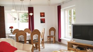 Un salon comprenant un canapé, un téléviseur, une table à manger avec des chaises et une fenêtre avec des rideaux.