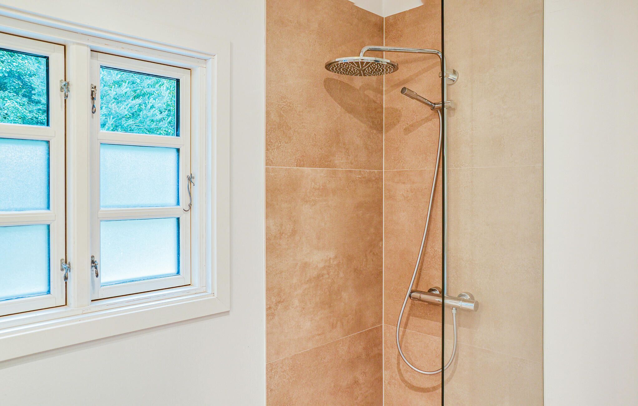 Ein Badezimmer mit Dusche, einem Fenster mit satinierten Gläsern und beigen Fliesen.