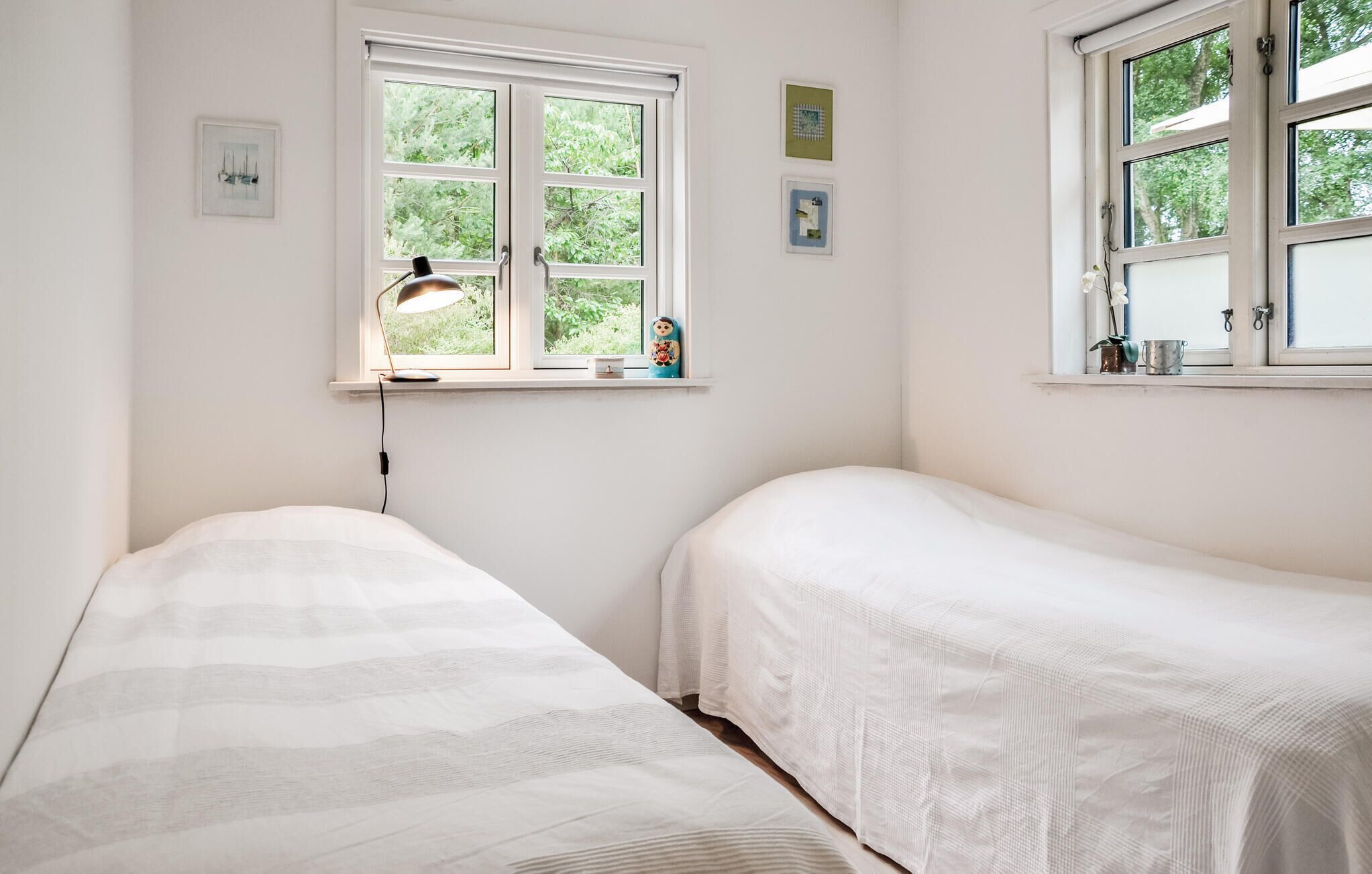 Une chambre avec deux lits simples, une fenêtre donnant sur un espace verdoyant et un bureau avec une lampe.