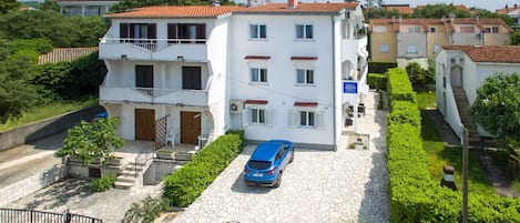 A two-story building with a stone-paved courtyard, a blue car parked in front, and a sign indicating a business on the ground floor.