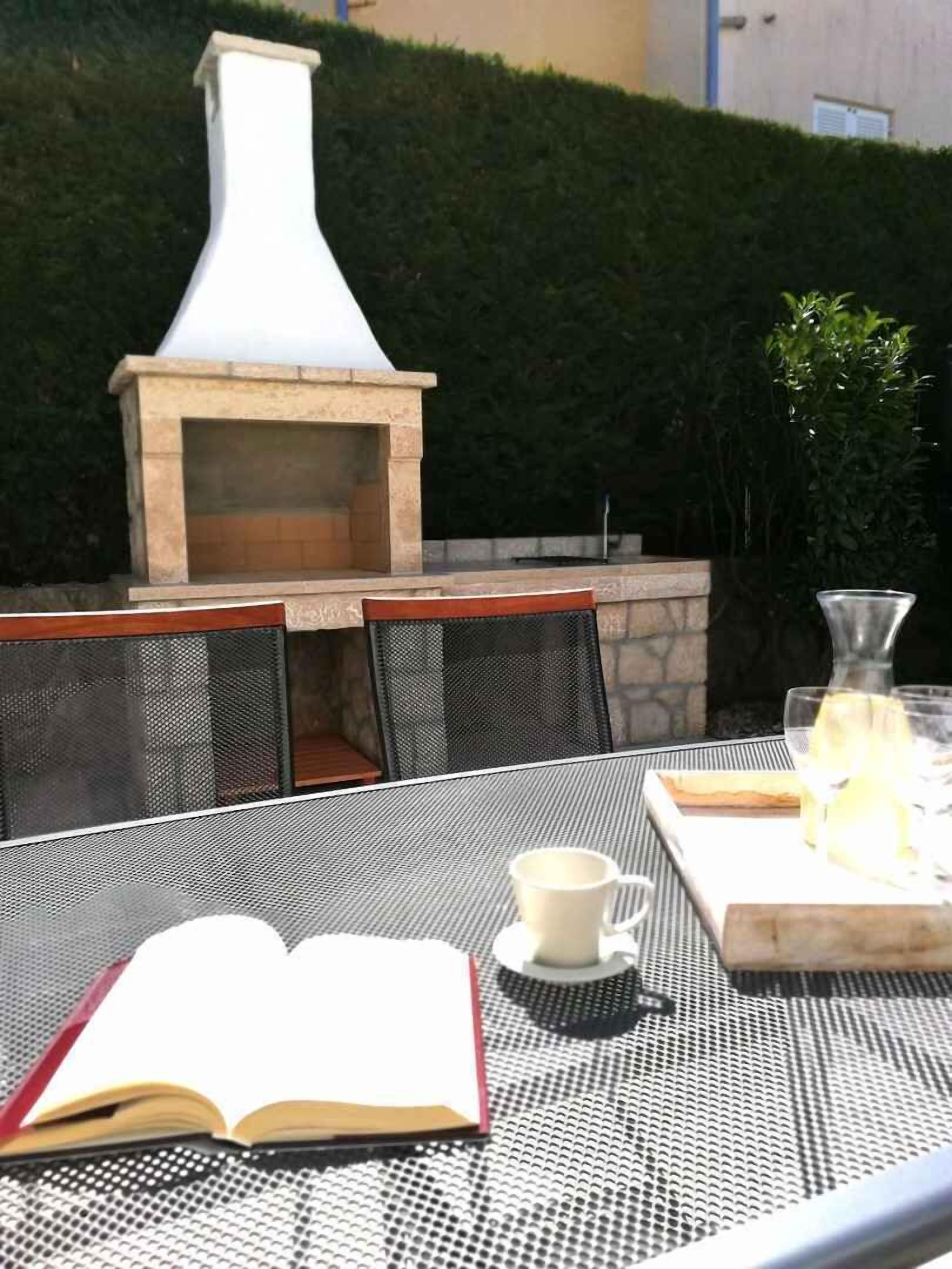 An outdoor dining area with a stone-built pizza oven, a table with chairs, and a book open on the table.