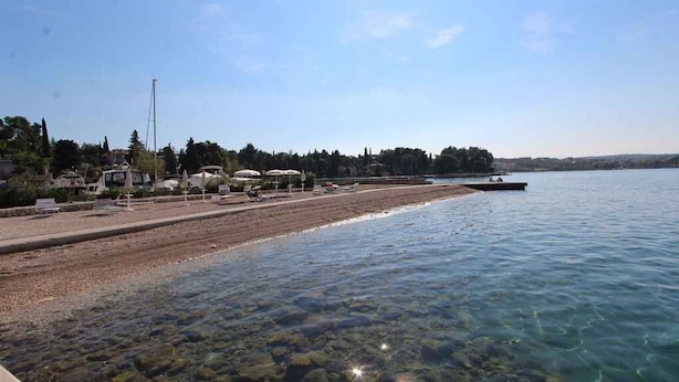 A beach with clear water, a sandy shore, and a boat in the distance.