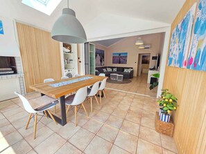 A modern kitchen with a built-in oven, a dining area with a wooden table and chairs, and a living room with a sofa and a painting.