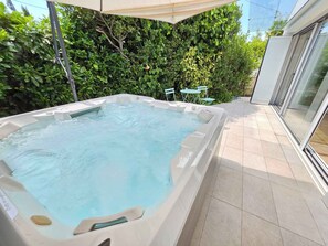 Ein Whirlpool mit einer gefliesten Terrasse, umgeben von viel Grün und einer Glastür zu einem Gebäude.