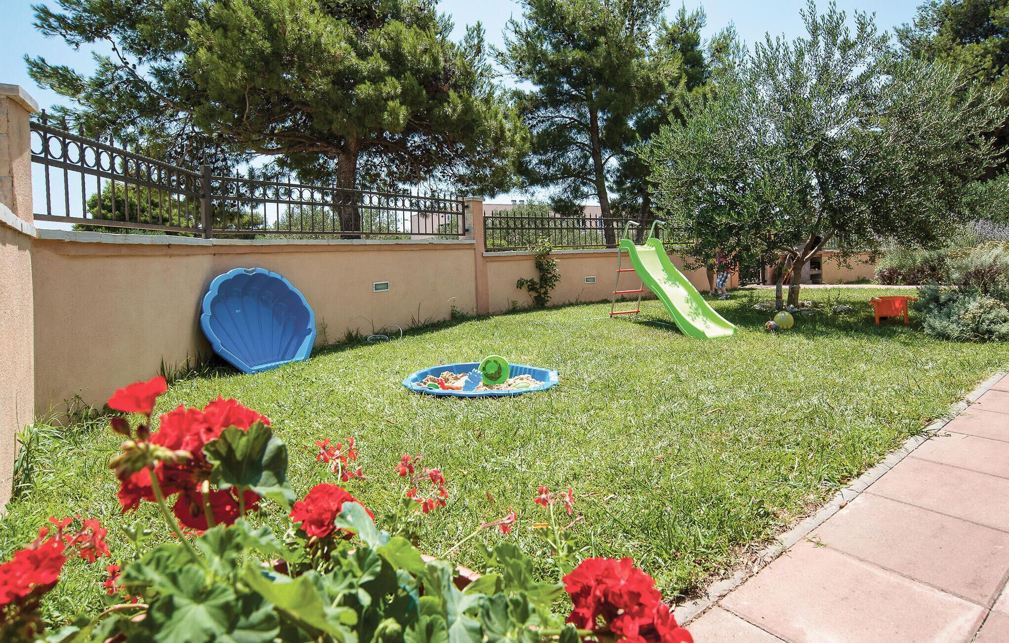 A backyard with a slide, a blue kiddie pool, and red flowers.