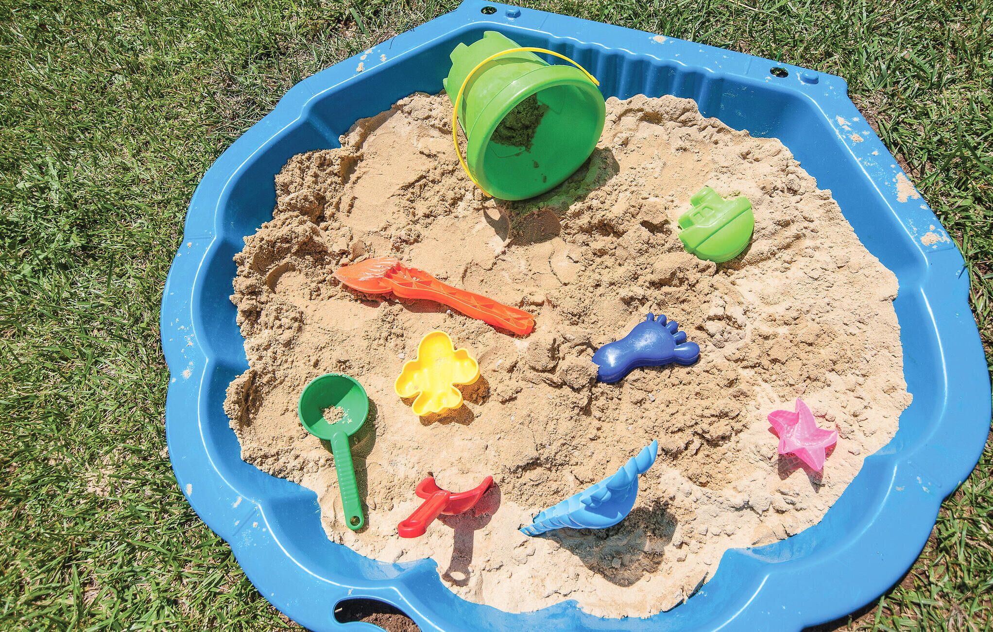 Um caixa de areia azul cheia de areia e diversos brinquedos de plástico coloridos.