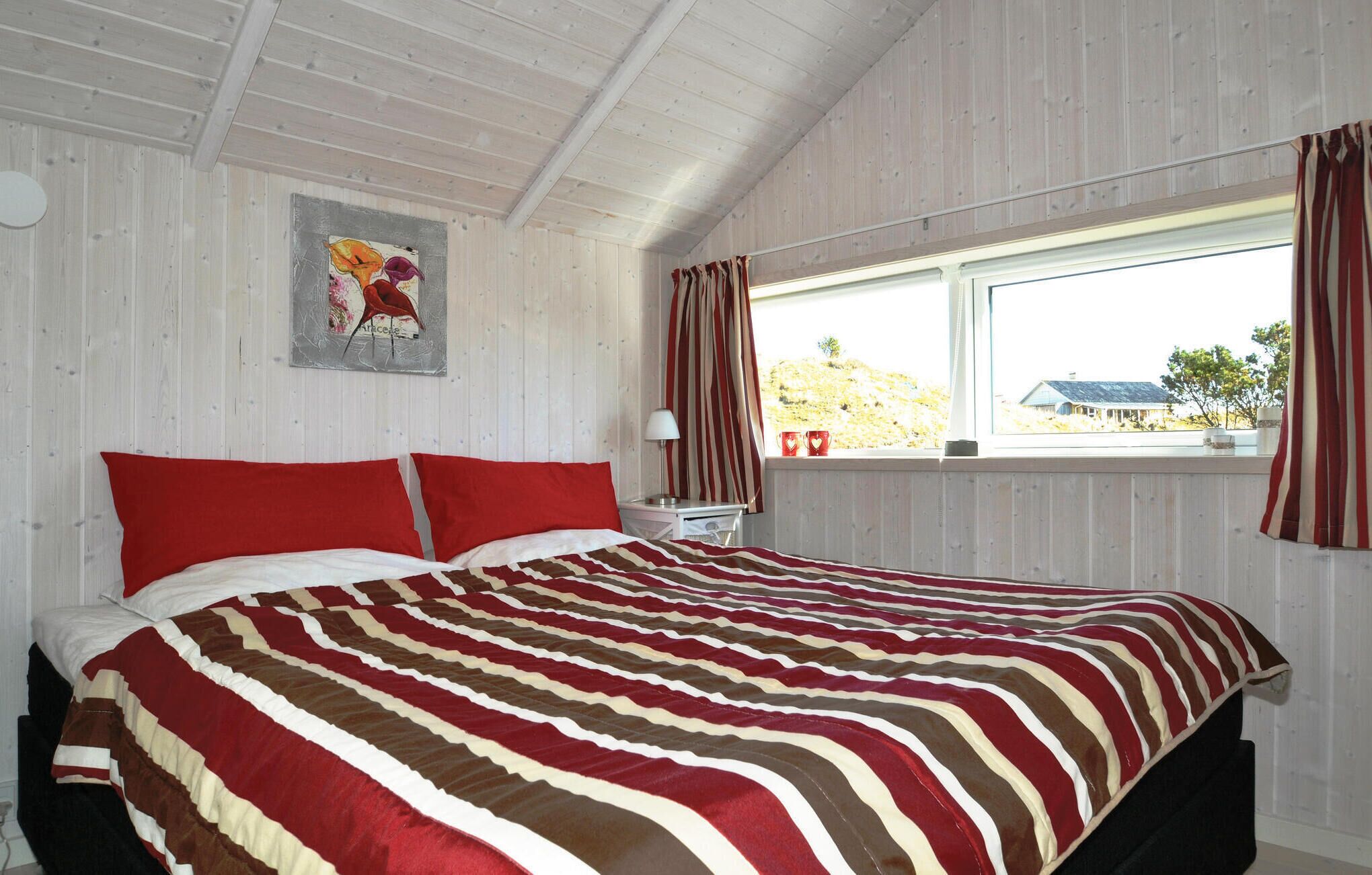Une chambre à coucher avec un grand lit, des rideaux à rayures, une fenêtre donnant sur une maison et un tableau accroché au mur.