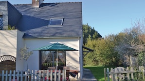 Ein Haus mit schrägem Dach, einem kleinen Fenster und einer Terrasse mit Tisch und Stühlen.