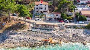 Un edificio costero con fachada de piedra, una terraza con asientos al aire libre y vistas al mar.
