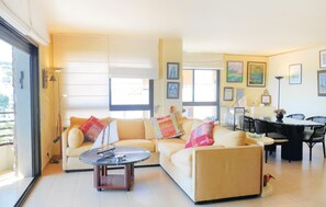 Relax in this stylish living room with a sofa, coffee table, and dining area, surrounded by large windows and artwork.
