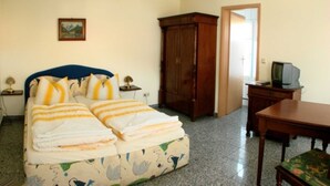 Un dormitorio con una cama, un armario de madera, un televisor sobre una mesa de madera y un cuadro en la pared.