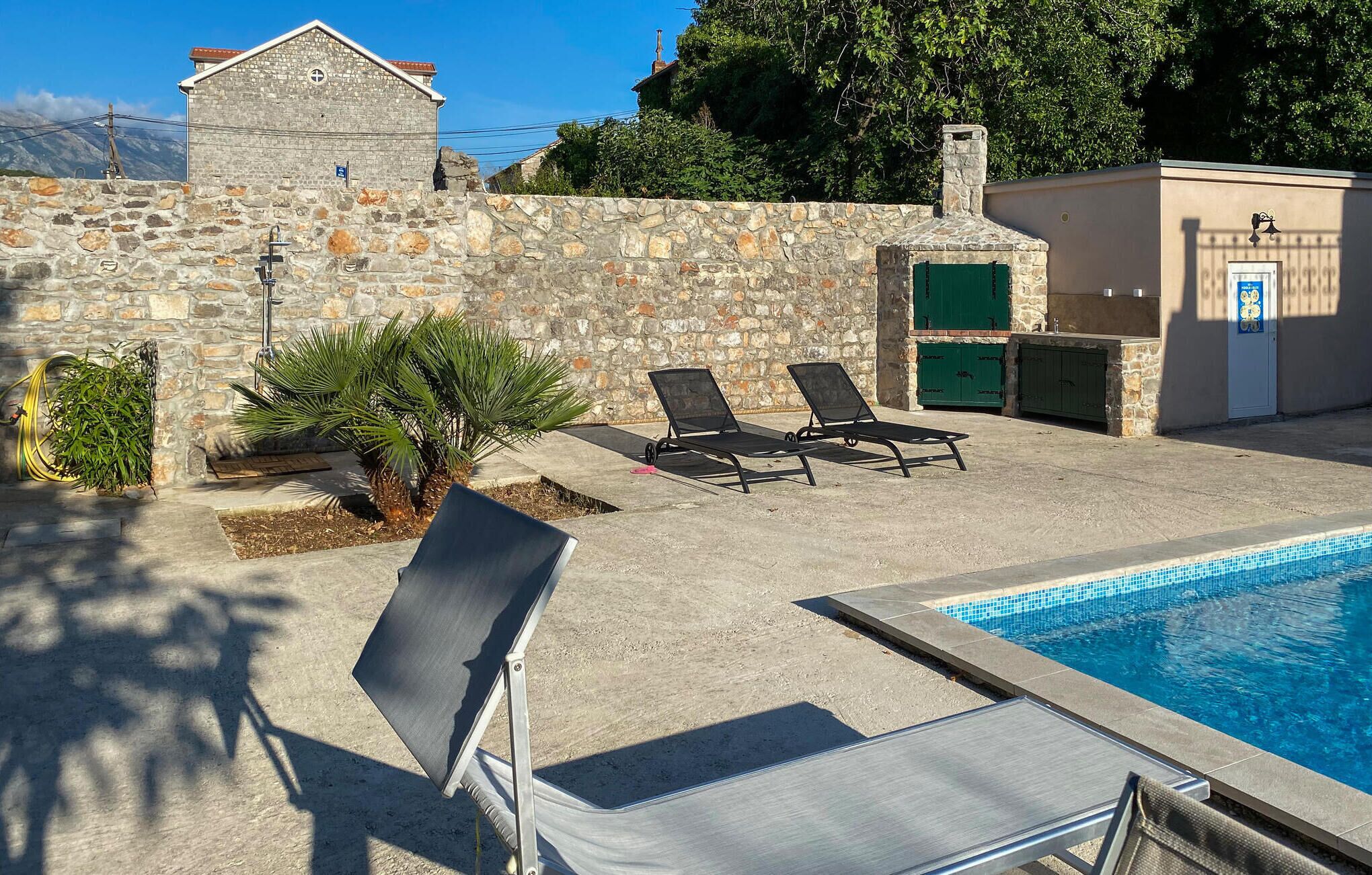 Un área de piscina con sillones de descanso, una pared de piedra y una pequeña palmera.