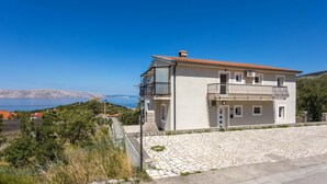 Ein zweistöckiges Gebäude mit Balkon, gepflastertem Vorplatz und Meerblick.