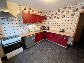 A compact kitchen with a gas stove, dishwasher, red cabinets, and a patterned backsplash.