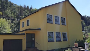 Um edifício amarelo de dois andares com garagem, escadaria e varanda com plantas em vasos.