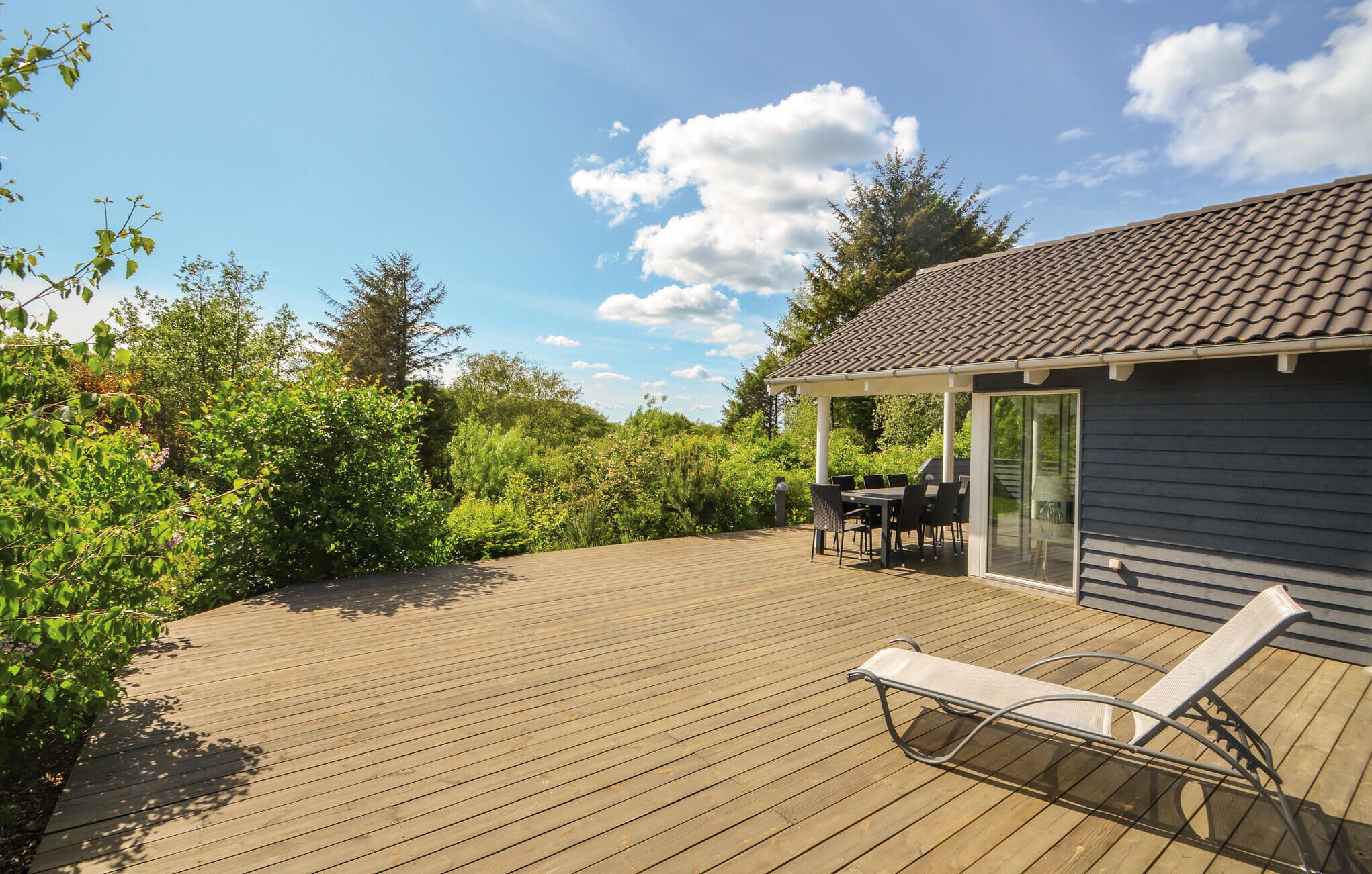 A wooden deck with a covered patio area, a lounge chair, and a table with chairs.