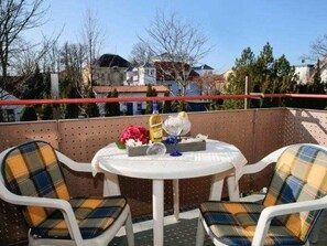 A balcony with two plaid chairs, a small round table, and a vase with flowers.