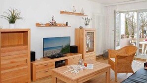 Una sala de estar moderna con muebles de madera, un televisor y un sillón de mimbre.