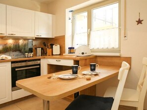 A compact kitchen with white cabinets, a wooden countertop, and a window with curtains. - (102) 2-room apartment - lake view - apartment complex Baltic Sea view (Kühlungsborn)