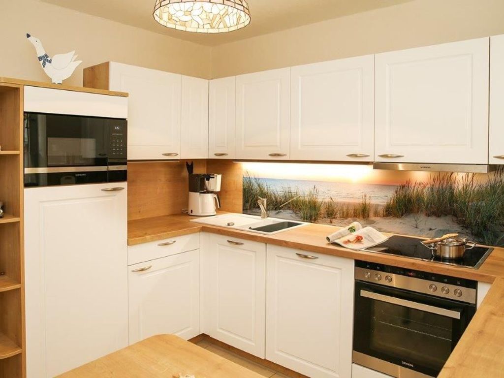 A modern kitchen with white cabinets, a built-in microwave, a stove, and a sink.