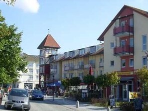 A multi-story building with balconies, a red-roofed tower, and a street in front. - (102) 2-room apartment - lake view - apartment complex Baltic Sea view (Kühlungsborn)