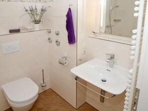 A bathroom with a white toilet, a sink, a shower, and a mirror with lights.