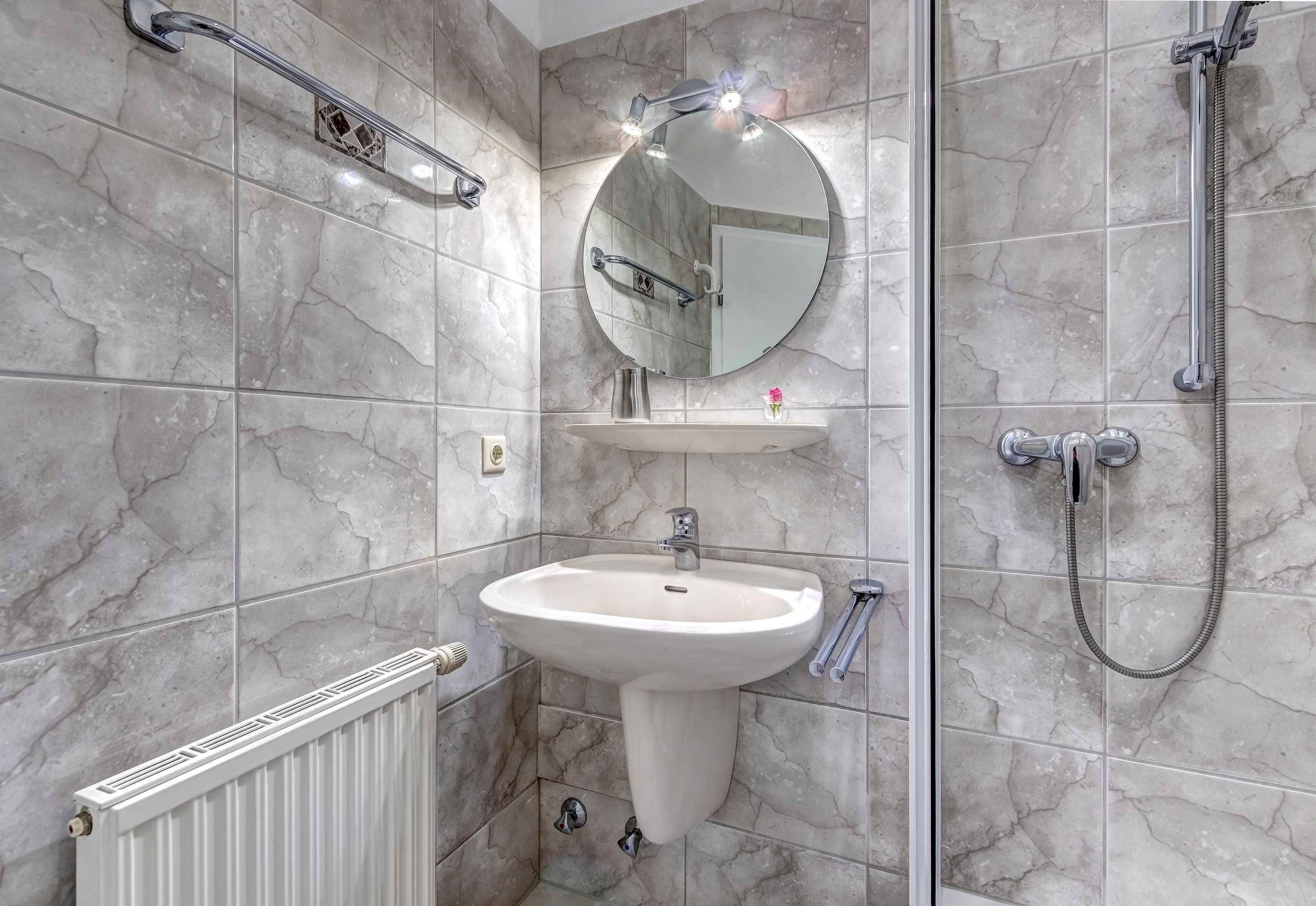 Ein Badezimmer mit einem Standwaschbecken, einem runden Spiegel, einer Handbrause und einem Handtuchhalter.