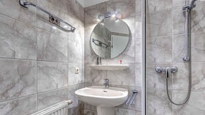 Ein Badezimmer mit einem Standwaschbecken, einem runden Spiegel, einer Handbrause und einem Handtuchhalter.