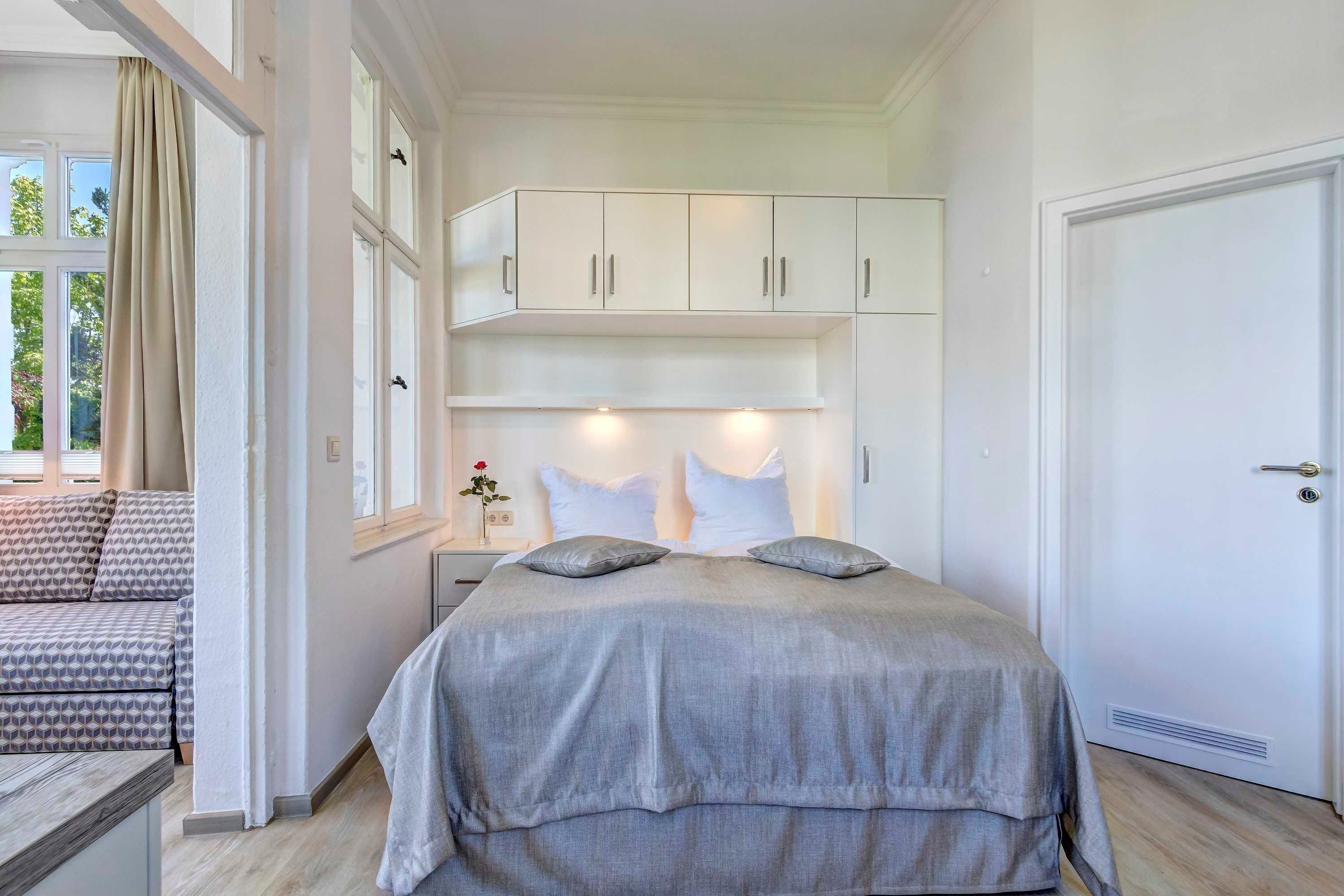 Un dormitorio con una cama grande, armarios blancos arriba y una puerta a la derecha.