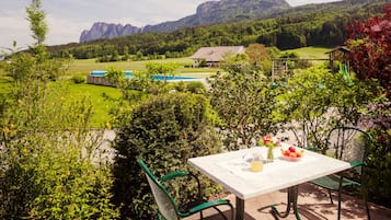 Eine Terrasse mit Tisch und Stühlen, Blick auf einen Berg und ein Gebäude im Hintergrund.
