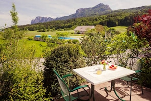 Eine Terrasse mit Tisch und Stühlen, Blick auf einen Berg und ein Gebäude im Hintergrund.