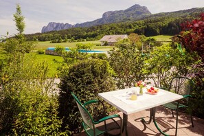 Un patio con una mesa y sillas, vista de una montaña y un edificio al fondo.