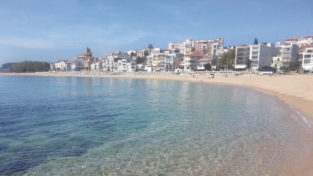 Un paysage urbain côtier avec une eau bleue et limpide, une plage de sable et un ensemble dense de bâtiments.