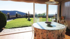 Une terrasse fermée par des baies vitrées, avec une table et des chaises, une fontaine décorative et une vue sur un paysage montagneux.