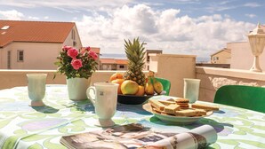 A table set with a fruit bowl, sandwiches, and a flower vase on a balcony with a city view. - Amazing apartment in Makarska with house sea view (Makarska)