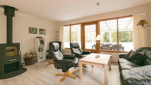 A cozy living room with a fireplace, leather chairs, a wooden table, and large windows offering a view of the outdoors. - 3 bedroom nice home in Nexø (Nexø)