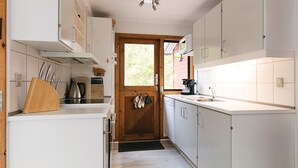 A compact kitchen with white cabinets, a wooden door, and a window. - 3 bedroom nice home in Nexø (Nexø)