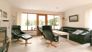 A modern living room with a wooden floor, a black leather sofa, two black leather chairs, a wooden coffee table, and a large window with curtains. - 3 bedroom nice home in Nexø (Nexø)