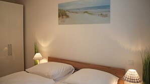 Un dormitorio con cama, armario, un cuadro de una playa y dos lámparas.