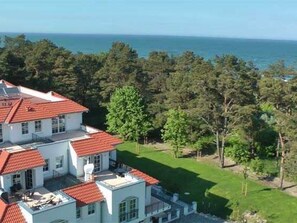Un edificio a più piani con tetto in tegole rosse, immerso nel verde e con vista sul mare.
