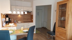 A modern kitchen with a dining area, including a table set for two, a coffee machine, and a cabinet with glassware. - Haus Meeresblick FeWo Strandkrabbe A 3.16 Ref. 159955 - FeWo Strandkrabbe A 3.16 (Baabe)