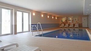 Una piscina interior con suelo de baldosas, una escalera de piscina y varias sillas de descanso.
